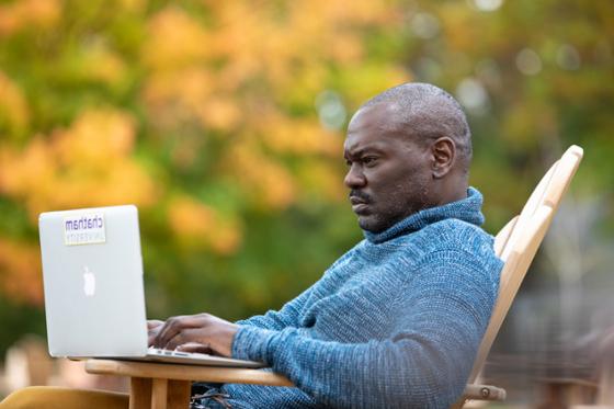 图为一名波胆网站的男学生在外面用笔记本电脑工作, with autumnal leaves in the background.